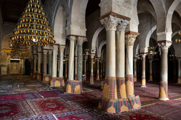 stock image Empty grand prayer hall of Great Mosque of Kairouan with rows of Corinthian columns, hanging chandeliers, and traditional carpets, Tunisia