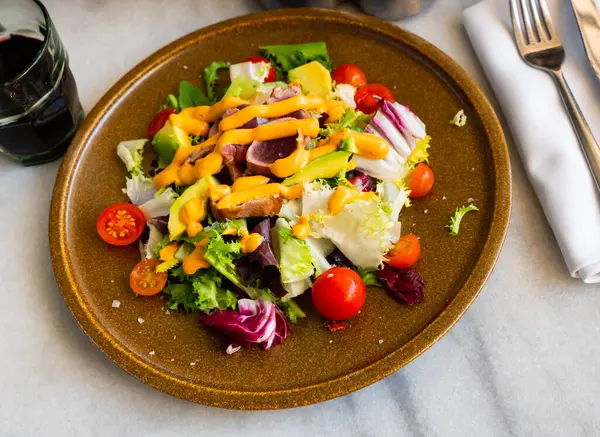 stock image Portion of a appetizing tataki tuna salad, avocado, corn, tomatoes and drizzled with sauce on top. Close-up image