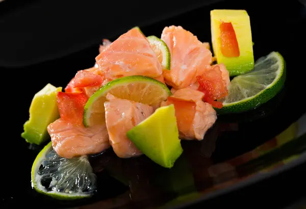 stock image Black plate with delicious salmon ceviche with avocado and lime