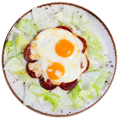 Homemade hearty breakfast - fried eggs with chorizo sausage. Dish is intricately decorated with slices of sausage. Large pieces of cabbage are laid out around dish. Isolated over white background clipart