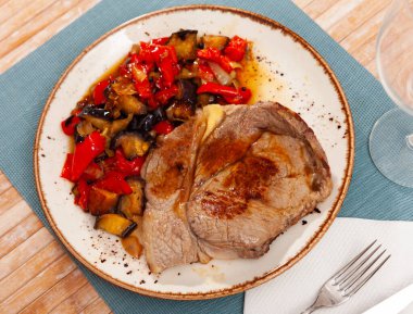 Piece of fried veal with stewed vegetables on white plate on table in restaurant clipart