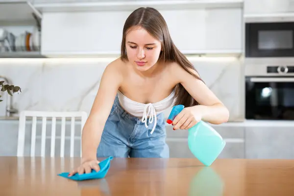 stock image Young woman wipes table with washcloth and disinfects kitchen surface. Lady wiping messy dirty cooking counter for housekeeping housework or chores.