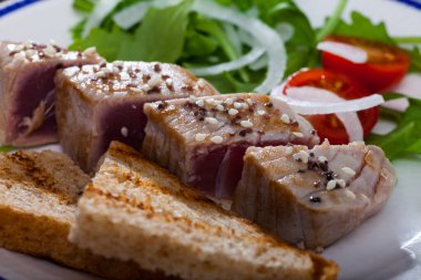 Slices of tuna fillet Tataki served with toasted bread, cherry tomatoes and greens clipart
