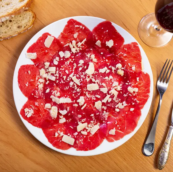 stock image Delicate slices of veal carpaccio topped with Parmesan shavings, presented on white plate for exquisite appetizer. Italian style cuisine