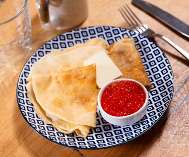 In center of shot - freshly baked pancakes with butter bowl of red grainy salmon caviar. Traditional Russian festive dish and snack clipart