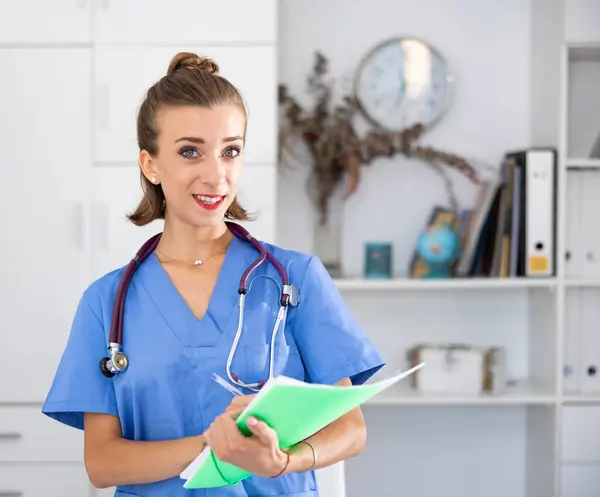 stock image Positive woman doctor in formal wear standing with folder in office