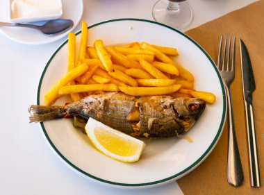 Appetizing whole roasted salema served with crispy French fries and lemon slice.. clipart