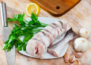 Image of fresh raw steaks of hake fish with greens and garlic on wooden background clipart