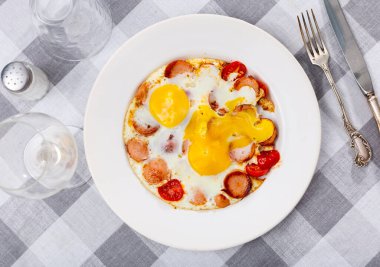 Homemade hearty breakfast - fried eggs with frankfurter and tomato. Dish is decorated by spring of cilantro parsley clipart