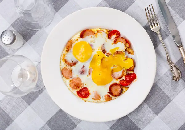 stock image Homemade hearty breakfast - fried eggs with frankfurter and tomato. Dish is decorated by spring of cilantro parsley