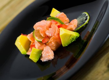 Image of delicious salmon ceviche with avocado and lime on black plate clipart