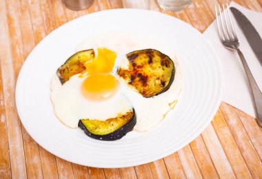 Plate with appetizing fried eggs, cooked with sliced and roasted eggplant clipart