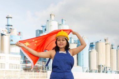 Teenage girl in blue overalls waving the flag of China against backdrop of a modern metallurgical plant clipart