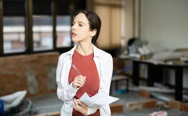 stock image Motivated young Spanish woman working on renovation and remodeling her house, making notes for space planning..