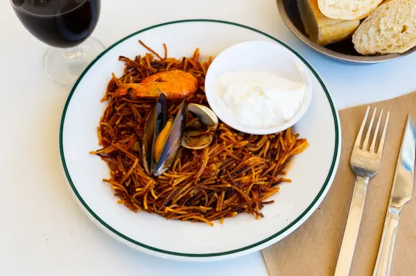 stock image Appetizing racy seafood fideua with shrimps, mussels, scallops and fish served on plate with spicy aioli sauce. Authentic Valencian cuisine