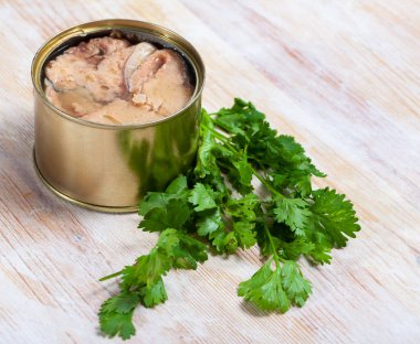 Open tin can of natural preserved pink salmon on wooden table with fresh parsley .. clipart