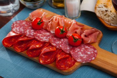 Appetizing cold cuts from Spanish ham and spicy dry-cured sausages with cherry tomatoes on wooden board.. clipart