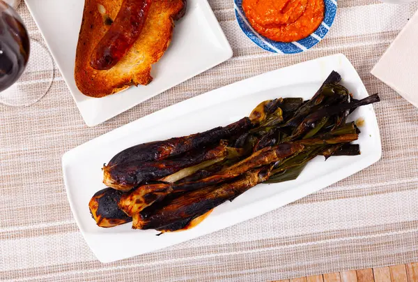 Stock image Roasted green onion, calcot, served on table with romesco sauce and botifarra.