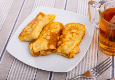 Delicious thin egg crepes stuffed with farmer cheese sweetened with sugar and vanilla served with cup of tea for brunch.. clipart