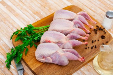 Four fresh raw quails with greens and spices prepared for cooking on wooden background.. clipart