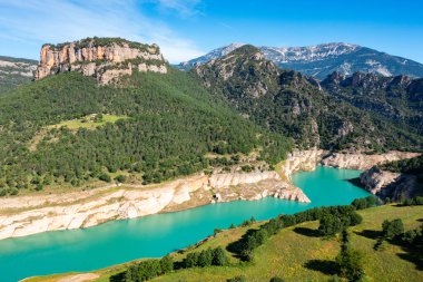 Scenic view of Llosa del Cavall reservoir, with turquoise waters, formed by dam on Cardener River in Spanish province of Lleida, framed by rocky Busa mountain range and lush greenery in summer clipart