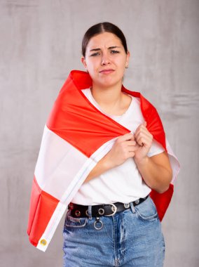 Sad young woman with Austria flag in hands posing sorrowfully against light unicoloured background clipart