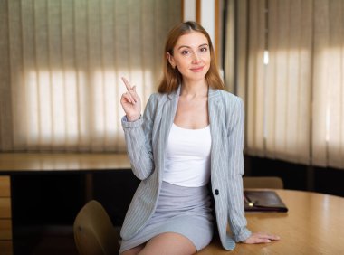 Portrait of a young sexy and confident businesswoman sitting on a table in a conference room clipart