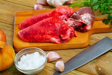 Ingredients for cooking. Raw mutton lungs and heart with onion, garlic, spices and herbs on wooden table clipart