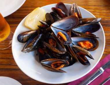 Steamed mussel with lemon on a white ceramic plate in a restaurant clipart