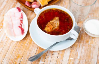 Borscht in bowl served on table with salo, garlic and smetana. clipart