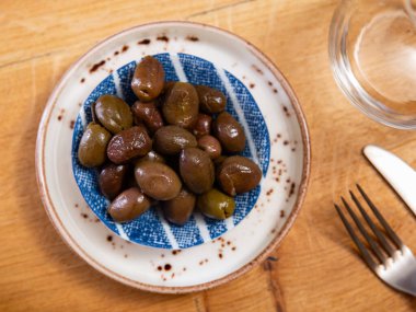 On small square white plate lies portion of large ripe green olives with stone. Snack is supplemented with glass of beer clipart