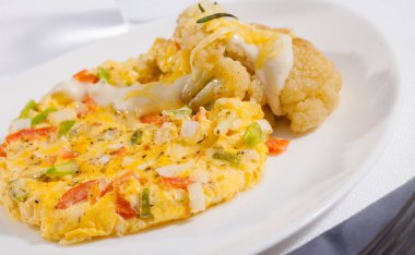 Delicious vegetable omelette served on white plate with cauliflowers, grated cheese and cream sauce.. clipart