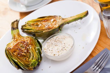 Delicious roasted halves of artichoke served with sea salt and sauce. Healthy vegetarian food.. clipart