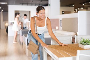 Happy woman near wooden table with drawers in the furniture store before the buying clipart