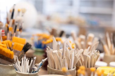 There are stands with pottery tools on table - sets of brushes, spatulas, hinges - close-up. Sets of tools for coloring and final processing of ceramic products. clipart