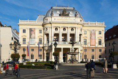 BRATISLAVA, SLOVAKIA - NOVEMBER 5, 2024: Main facade of Bratislava National Theatre. Passers-by pedestrians look at posters of theater. clipart