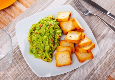 Guacamole with dry bread served on plate in restaurant. Avocado-based dish. clipart