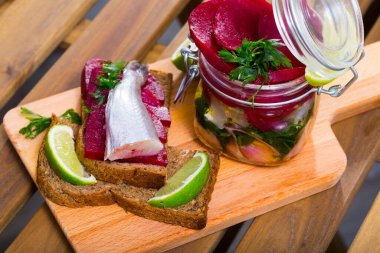 Jar of homemade marinated Micromesistius poutassou fish with onion, beetroot, lime juice and olive oil clipart