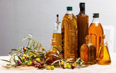 Bottles and carafes with olive oil and fresh olives on wooden table. Ingredients for cooking clipart