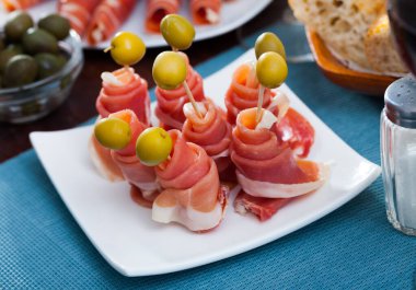 Delicious Spanish ham served as rolls with green olives on white plate.. clipart