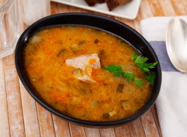 Pickle soup with pearl barley, potatoes, onions, carrots and parsley. Rassolnik in a white plate on a marble background. Traditional dish of Russian cuisine. Top view clipart