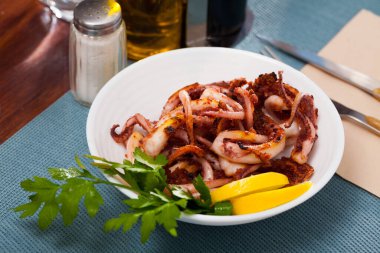 Seafood appetizer. Fried octopus tentacles garnished with greens and lemon.. clipart