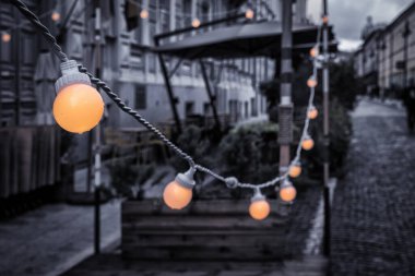 Yazlık kafe terası. Geçen akşam, mevsimin sonunda. Ampuller ısınacak. Seçici odak.