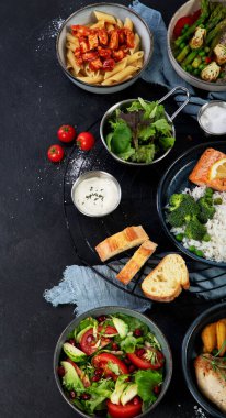 Bir dizi ana yemek. Farklı sağlıklı ana yemekler, et ve balık yemekleri, makarna, salatalar, soslar, arka planda ekmek ve sebzeler. Üst görünüm.