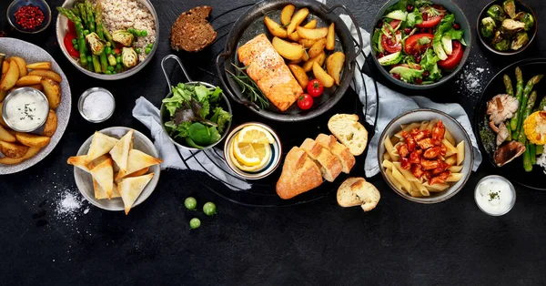 様々なメイン料理のセット 異なる健康的なメインコース 肉や魚料理 パスタ サラダ ソース 暗い背景にパンや野菜 トップビュー パノラマ — ストック写真