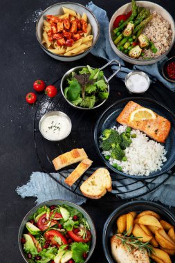 Bir dizi ana yemek. Farklı sağlıklı ana yemekler, et ve balık yemekleri, makarna, salatalar, soslar, arka planda ekmek ve sebzeler. Üst görünüm.