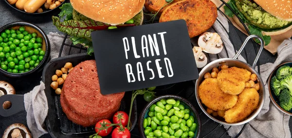 Stock image Plant-based food concept-vegan burgers, sausages, vegetarian nuggets, fresh vegetables and sauces on a dark background. top view. Panorama.