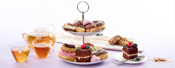 Traditional English tea. Afternoon tea with  selection of sweets  on violet background. Holiday concept, panorama, banner