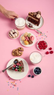 Üzerinde çeşitli kurabiyeler, çörekler, kekler, peynirli kekler ve pembe arka planda kahve fincanları olan masa. Lezzetli tatlı masası. Üst görünüm