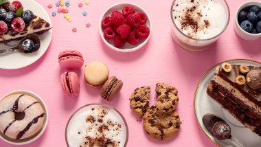 Üzerinde çeşitli kurabiyeler, çörekler, kekler, peynirli kekler ve pembe arka planda kahve fincanları olan masa. Lezzetli tatlı masası. Üst manzara, düz uzanma